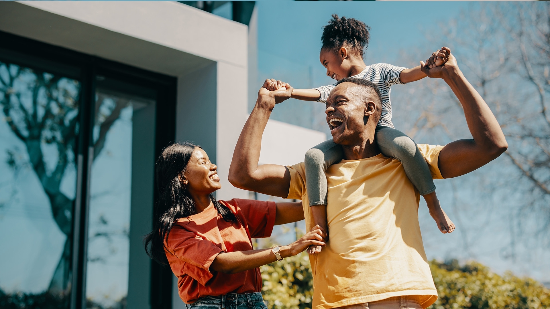 A family having fun outside, with the father giving his daughter a piggyback ride.