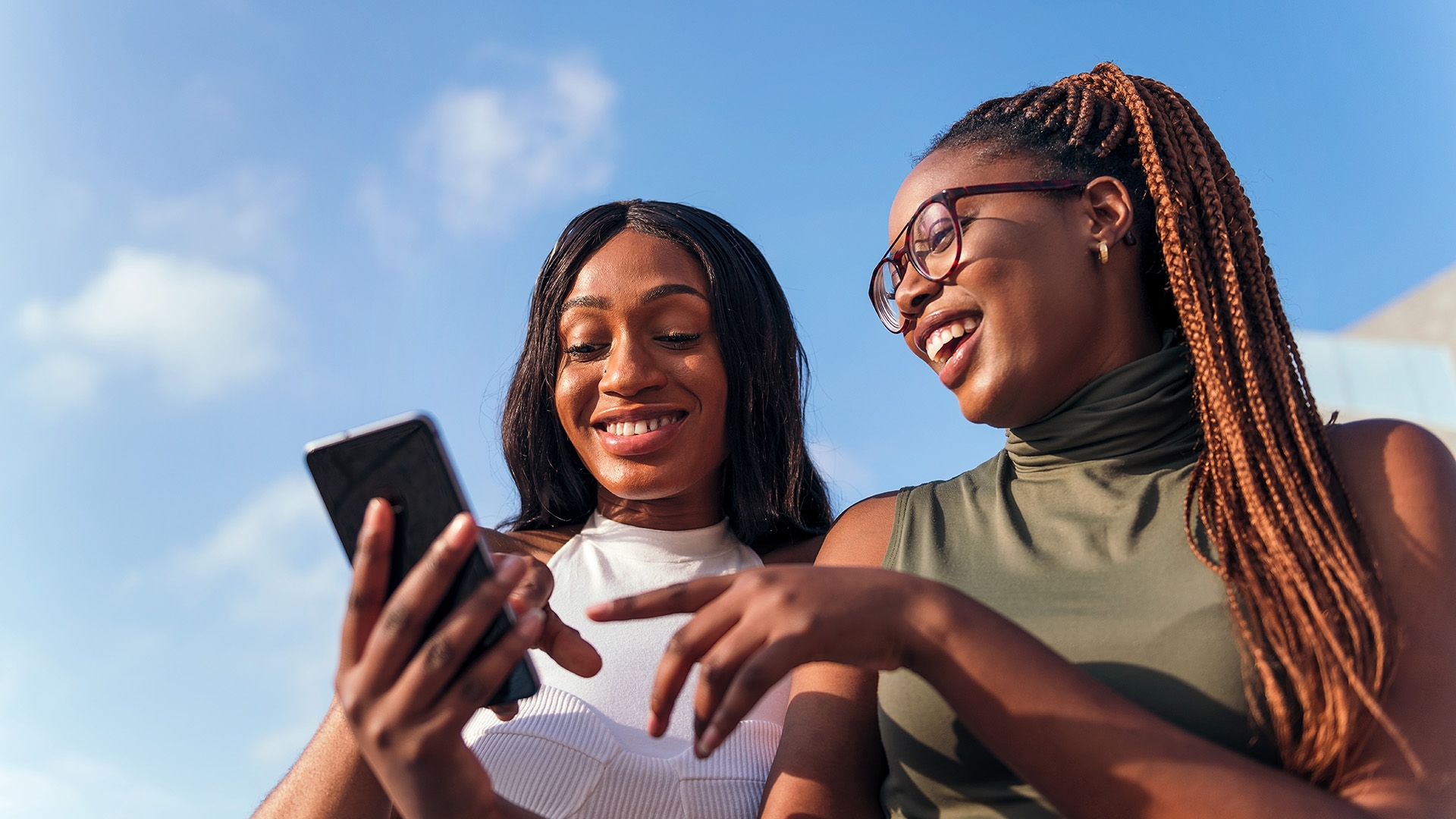 Two teenage girls looking at a phone and laughing.