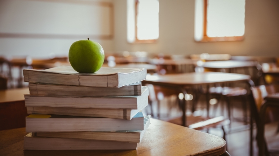 An apple sitting on top of a stack of books in a classroom.