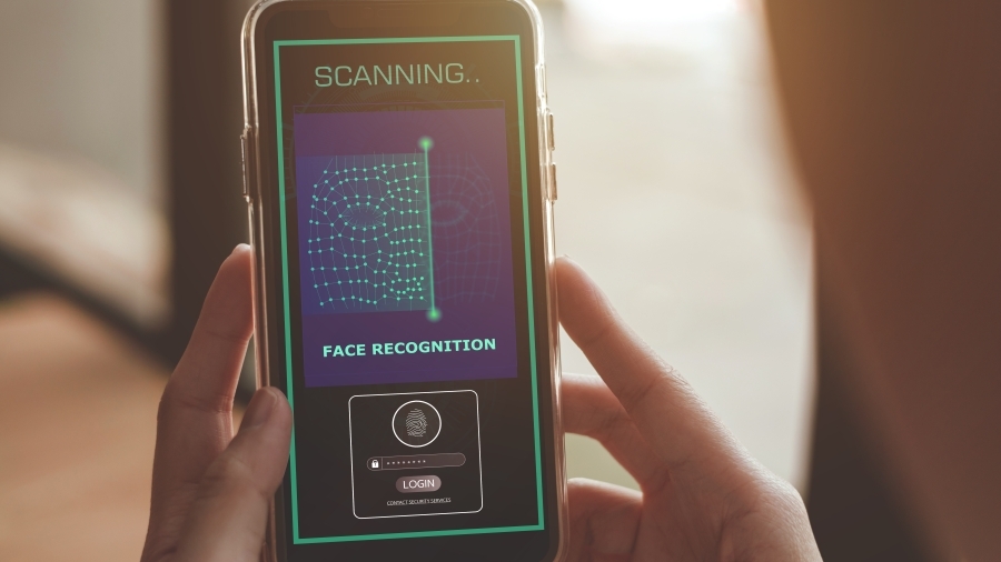 A photo of somebody holding a smart phone, which is scanning their face. Text on the phone says "face recognition."