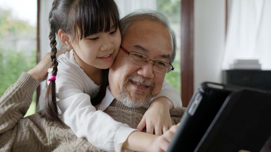 A grandfather and granddaughter looking at a screen together.