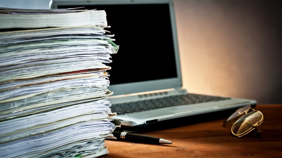 A stack of files next to a laptop.