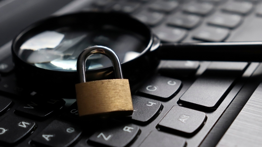 A magnifying glass and a lock sitting on top of a computer keyboard.