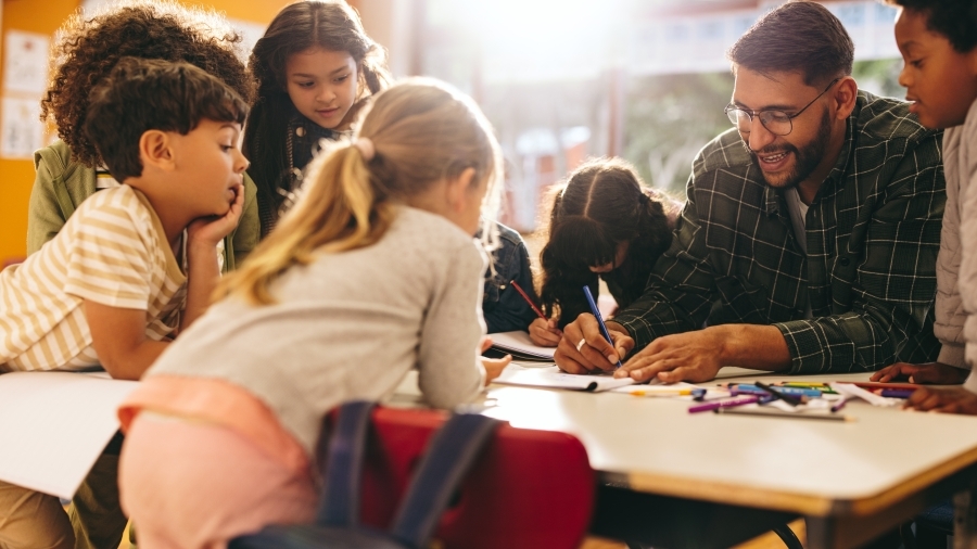 A teacher and a group of students sit around a table.