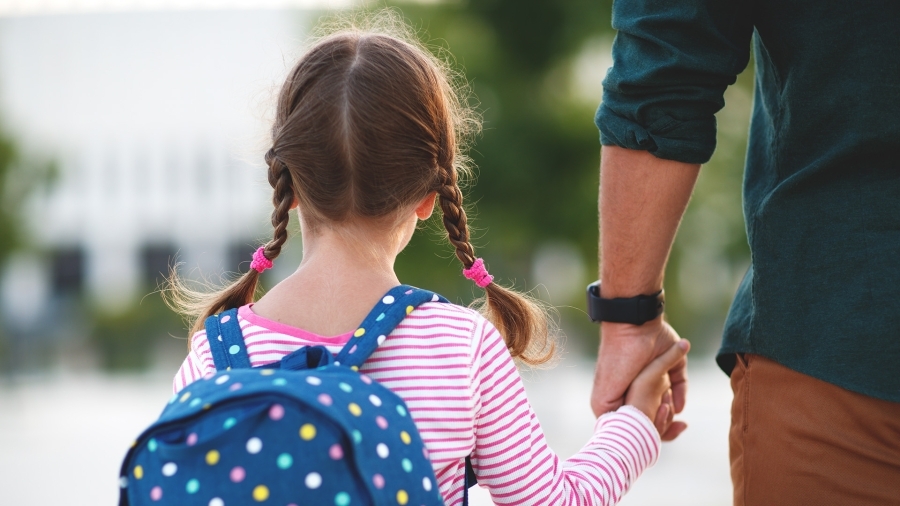 A young girl holding her parent's hand on the way to school.