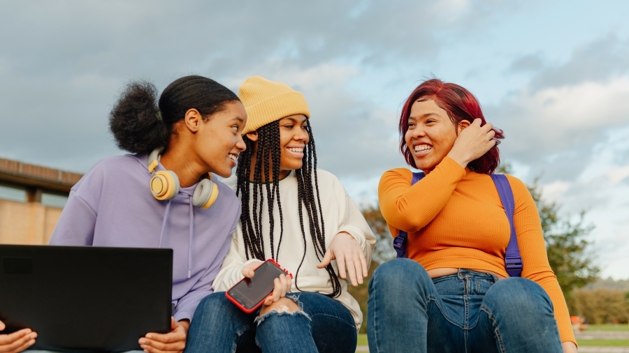 A group of three teens laughing while sitting on some steps.