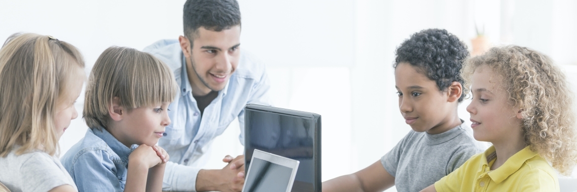 Man informing group of four children using computer.