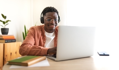 Man sitting at laptop computer working and smiling with headphones on.